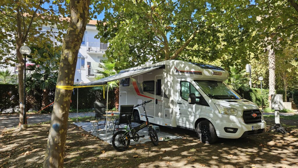 Challenger 287GA matkailuauto markiisi auki leirintäalueella puiden varjossa